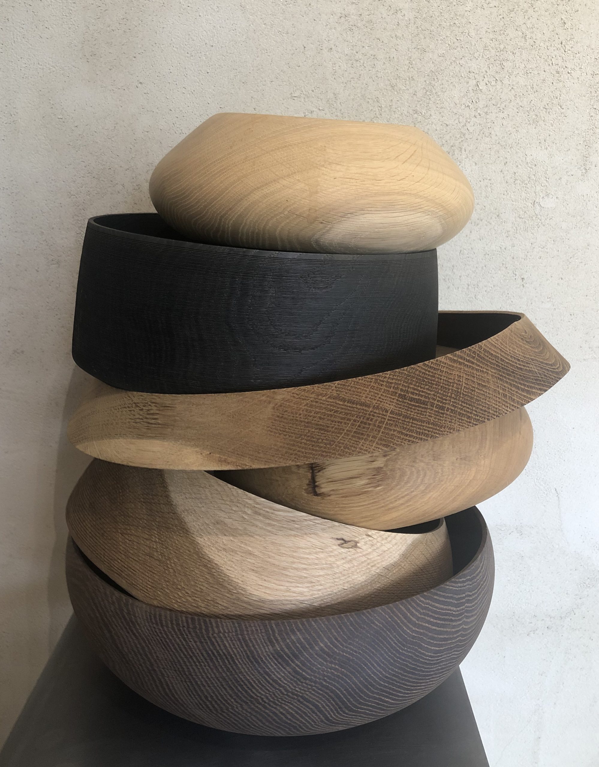 Gestapelte handgedrechselte Holzschalen in verschiedenen Farbnuancen und Formen aus Eiche und Nussbaum, präsentiert vor gespachtelter Wand – skulpturales Wohnaccessoire mit natürlicher Haptik