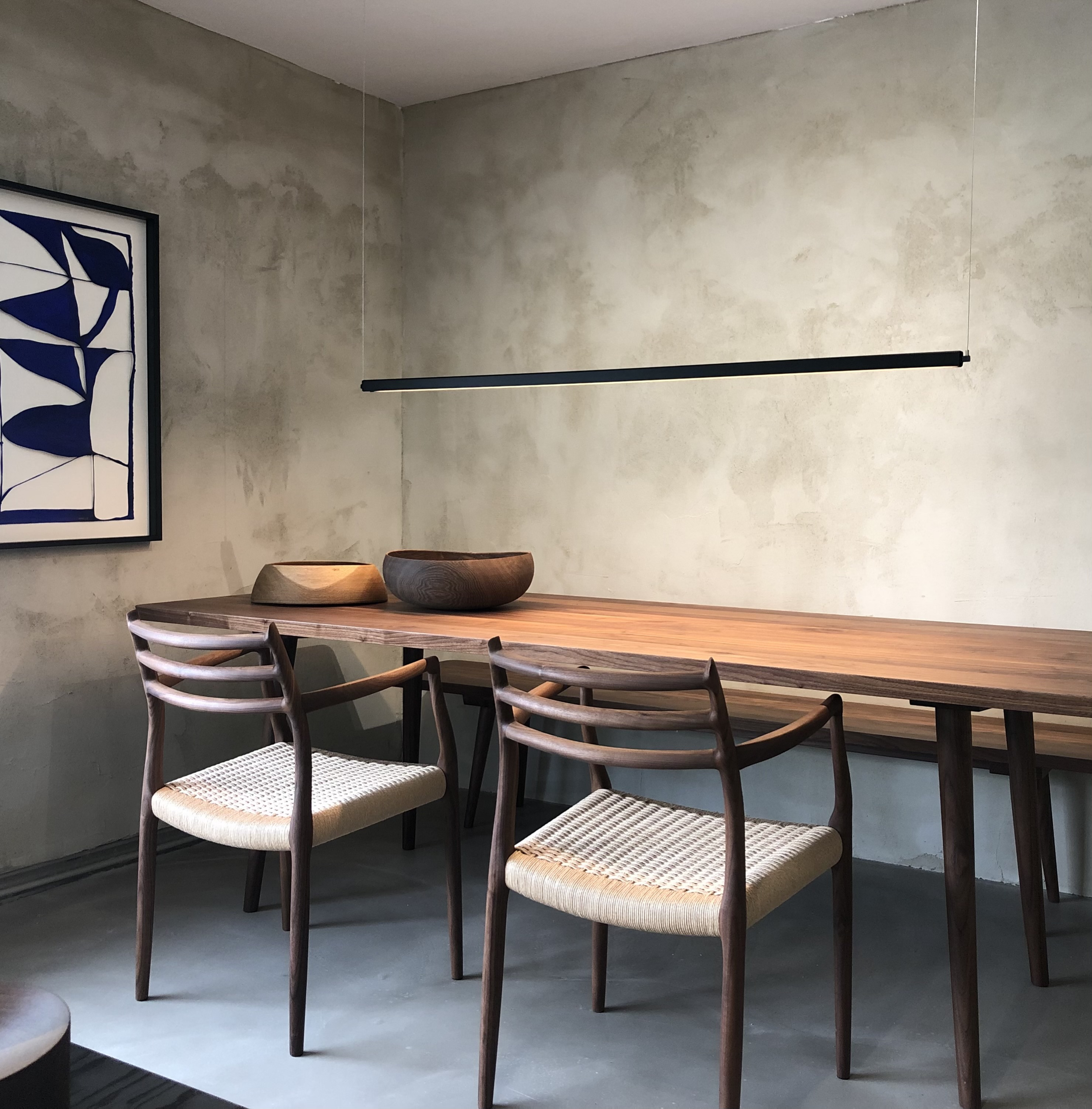 Essbereich mit Massivholztisch aus Nussbaum, skandinavischen Stühlen mit Papiergeflecht, linearem Pendelleuchten-Design und handgedrechselten Holzschalen vor gespachtelter Kalkputzwand